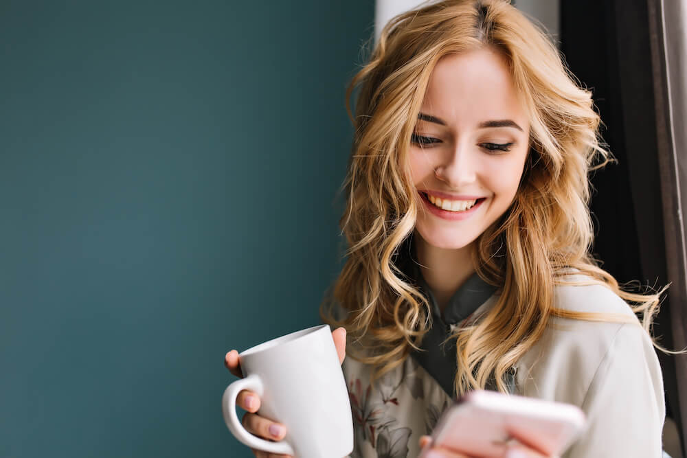 smiling woman holding coffee and phone